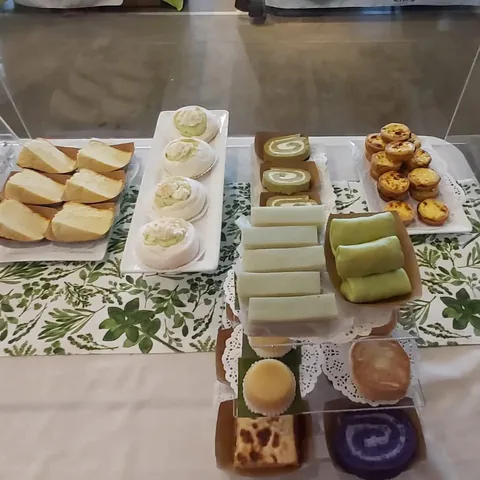 Market table with cake slices, pavlova nests, green rolls and egg tarts on a leaf-print cloth