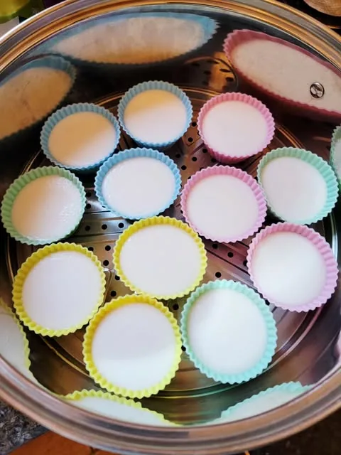 Round silicone cups of coconut custard steaming in a steel steamer